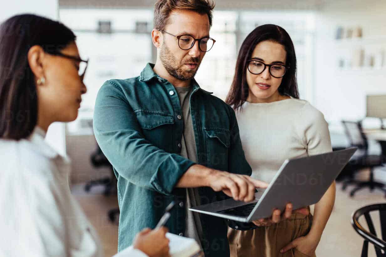 Group of business people using a laptop and having a discussion in an office. Team of business professionals standing together and having a meeting.
